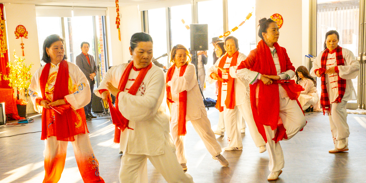 Women in white clothing and a red scarf perform a traditional dance.