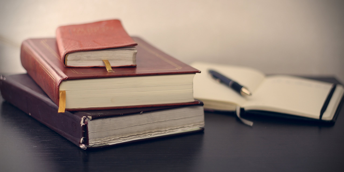 Old looking books and an open notepad with a pen on it