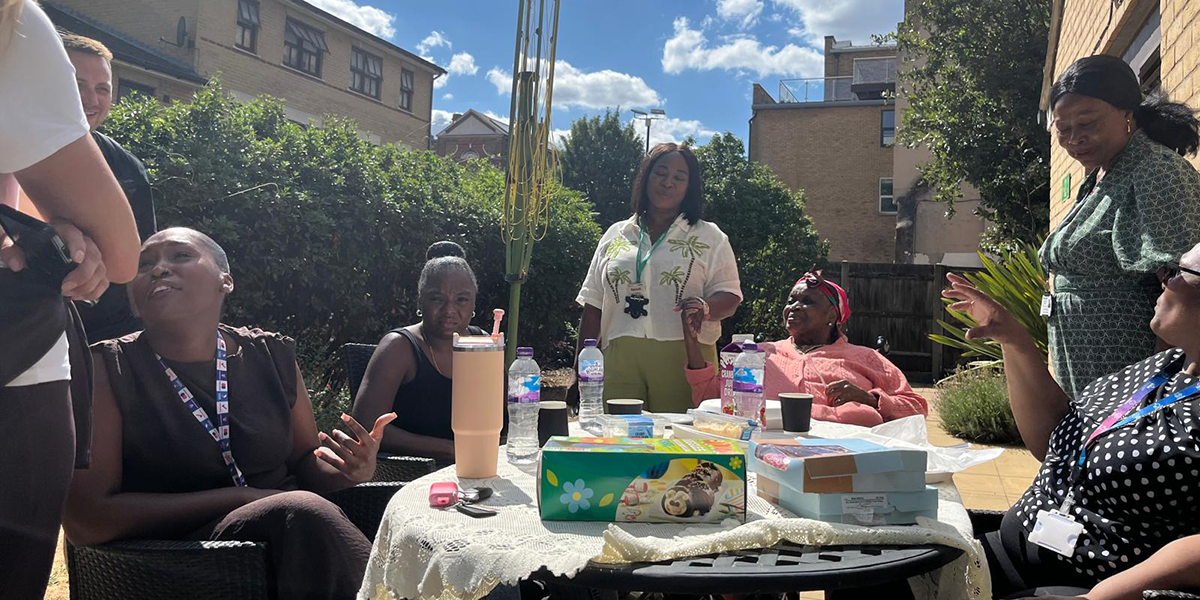 People are sat around a table in the garden smiling and sharing food.