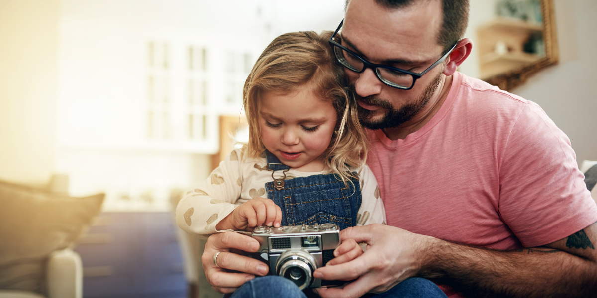 A man teaches a young girl how to use a camera. 