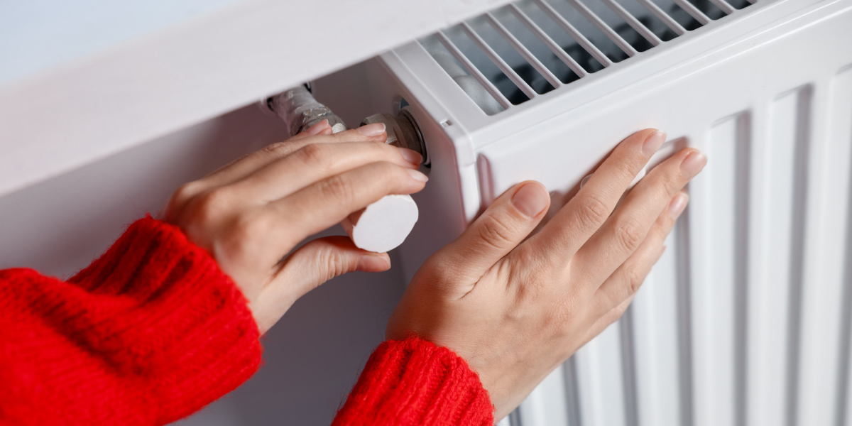 a woman wearing a red jumper is adjusting the temperature on her radiator