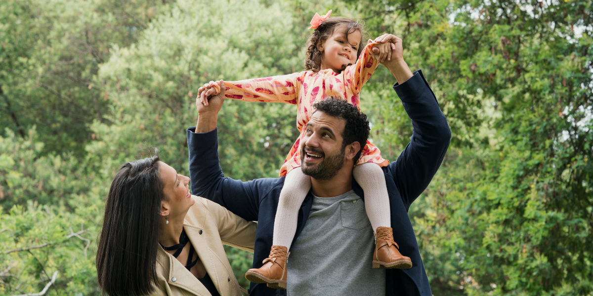 A father carries his daughter on his shoulders on a walk in the park. 