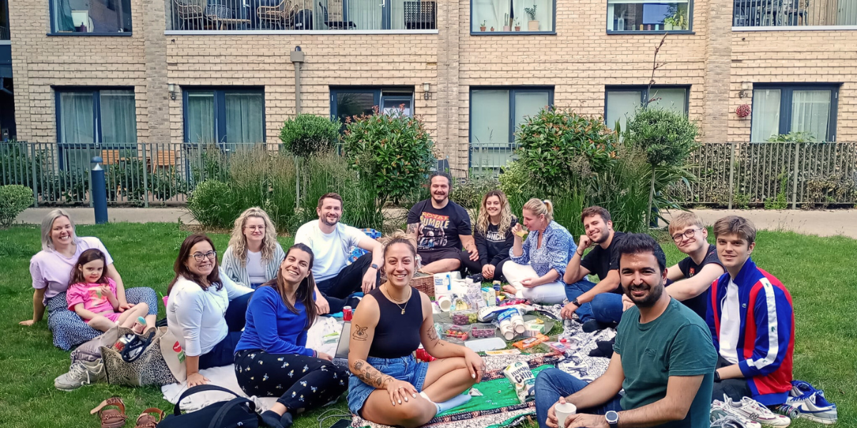 Residents have a picnic on a green space by their building. 