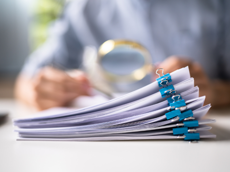 Someone holds a magnifying glass over a stack of documents. 