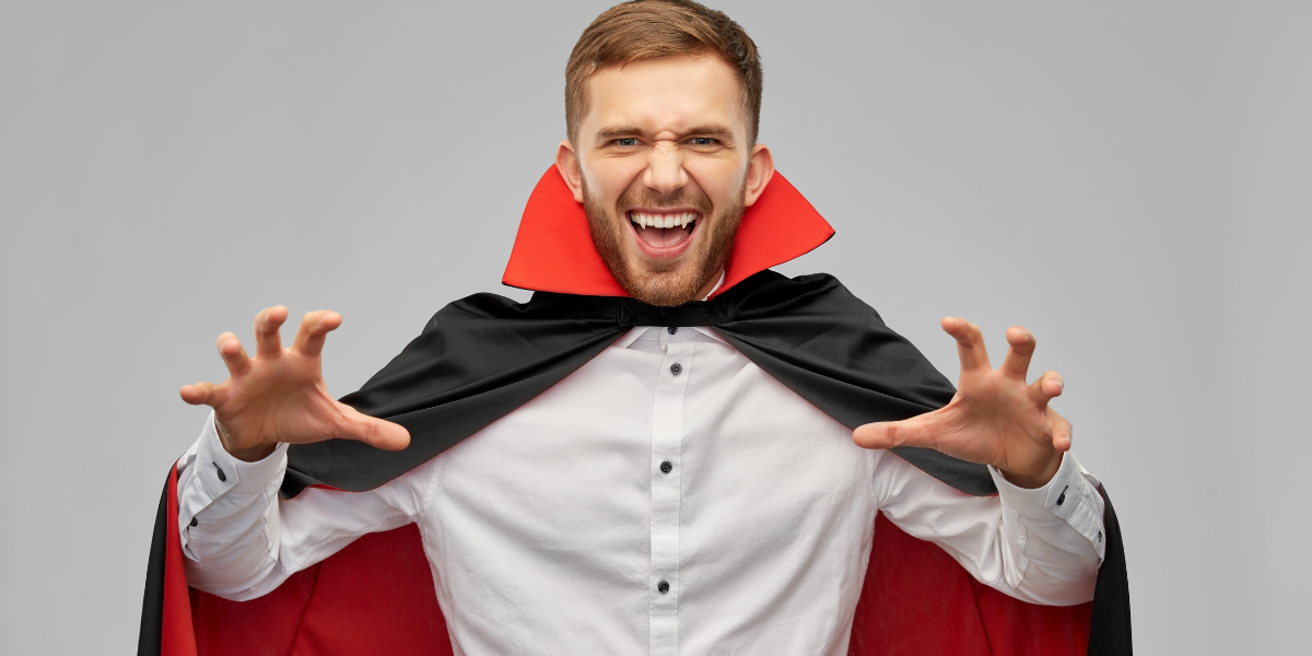 A man dressed as a vampire with his fangs showing.