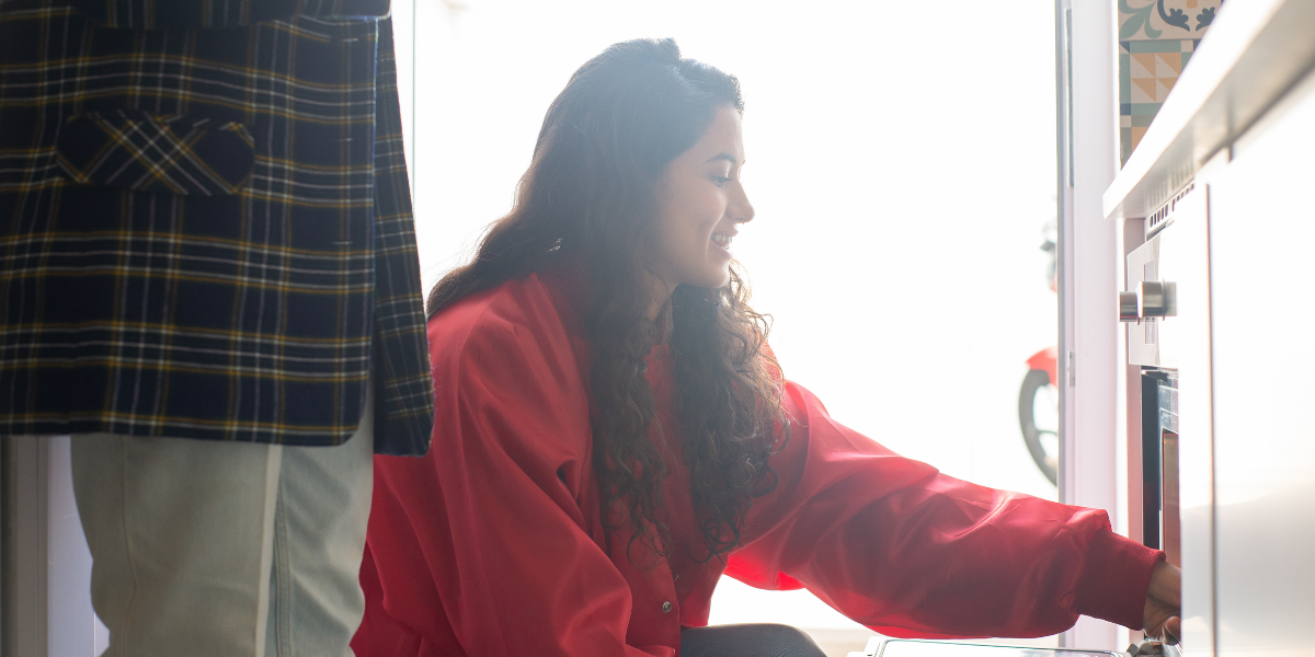 A smiling woman uses an oven.